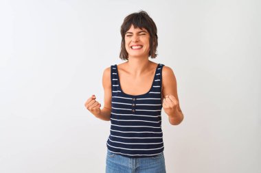 İzole edilmiş beyaz arka plan üzerinde duran çizgili tişört giyen genç ve güzel bir kadın mutlu ve heyecanlı bir şekilde kollarını kaldırıp, gülümseyerek ve başarı için çığlık atarak zafer hareketi yapıyor. Kutlama konsepti.