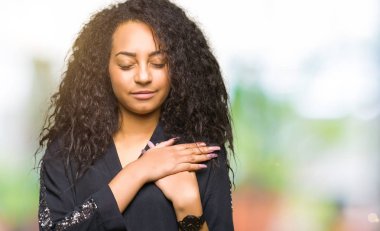 Kıvırcık saçlı kapalı gözler ile göğüs ellerinde ve yüzünde minnettar jest ile gülümseyen zarif elbise genç güzel kız. Sağlık kavramı.