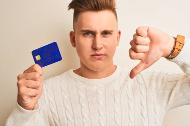 Genç, yakışıklı bir adam kredi kartını izole edilmiş beyaz arka planda tutuyor. Kızgın bir yüzü var. Negatif işaretleri var.