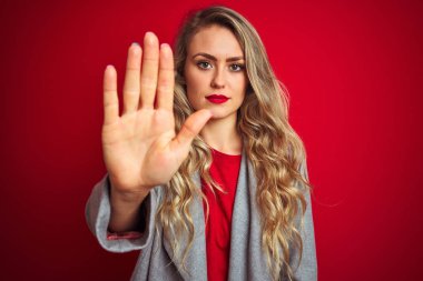Güzel bir iş kadını kırmızı izole edilmiş arka planda duran zarif bir ceket giyiyor ve avucunun içi gibi şarkı söylemeyi kesiyor. Yüzünde olumsuz ve ciddi bir jest olan uyarı ifadesi.