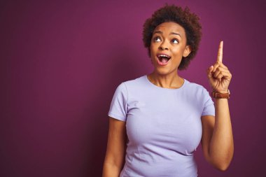 İzole edilmiş mor arka plan üzerinde saçı olan güzel Afro-Amerikalı kadın başarılı bir fikir işaret ediyor. Heyecanlı ve mutlu. Bir numara..