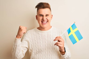 İsveçli yakışıklı genç adam izole edilmiş beyaz arka plan üzerinde İsveç bayrağı tutuyor. Gururla bağırıyor, zaferi ve başarıyı kutluyor. Çok heyecanlı, coşkulu bir duygu.