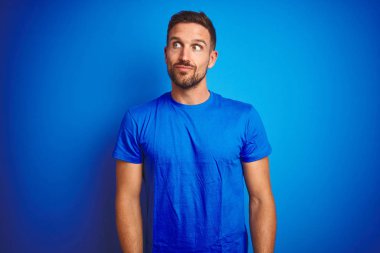 Mavi izole edilmiş arka planda sıradan tişörtler giyen genç yakışıklı adam gülümsüyor ve başka yöne bakıyor..