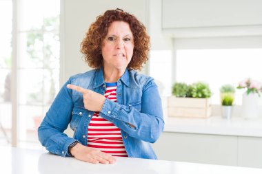 Evde kıvırcık saçlı, kot ceket giyen orta yaşlı bir kadın endişeli, endişeli ve şaşırmış bir ifade takınıyor.