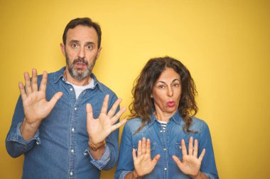 Güzel bir orta yaşlı çift, izole edilmiş sarı arka planda dikiliyorlar. Avuçlarını kaldırıyorlar. Korkmuş ve iğrenç bir ifadeyle reddedip inkar ediyorlar. Dur ve yasakla.