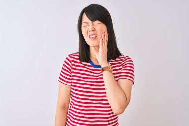 İzole edilmiş beyaz arka plan üzerine kırmızı çizgili tişört giyen genç ve güzel Çinli bir kadın diş ağrısı ya da diş ağrısı yüzünden ağız ve acı dolu bir ifadeyle dokunuyor. Dişçi konsepti.