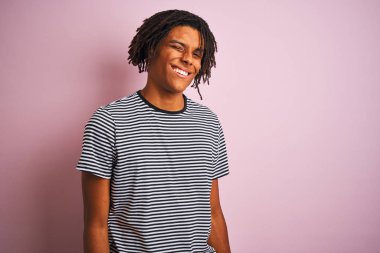 Saçlı, denizci çizgili tişörtlü bir Afro adam izole edilmiş pembe arka planda duruyor ve kameraya seksi bir ifadeyle bakıyor. Neşeli ve mutlu bir yüzü var..