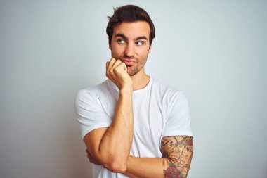 İzole edilmiş beyaz arka plan üzerine gündelik tişört giyen genç ve yakışıklı bir adam elleri ağız yiyen tırnaklarla stresli ve gergin görünüyor. Endişe sorunu.