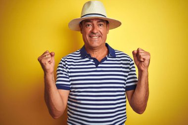 Çizgili polo giyen yakışıklı orta yaşlı bir adam ve izole edilmiş sarı arka plan üzerinde şapkası var. Kollarını kaldırarak ve açık gözlerle başarıyı kutluyor ve şaşırıyor. Kazanan konsept.