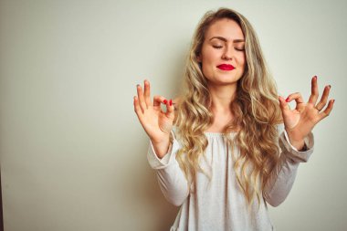 Genç ve güzel bir kadın izole edilmiş beyaz arka planda duruyor rahatla ve gülümse gözleri kapalı parmaklarıyla meditasyon hareketi yapıyor. Yoga konsepti.