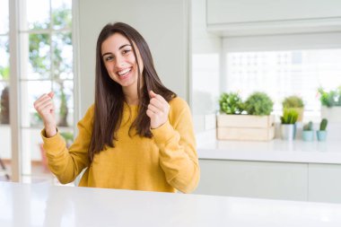 Sarı kazak giyen güzel genç kadın çok mutlu ve heyecanlı silah kaldırdı, gülümseyen ve başarı için çığlık ile kazanan jest yapıyor. Kutlama konsepti.