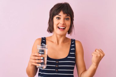 Genç ve güzel bir kadın pembe arka planda dikilip gururla haykırıyor zaferi ve başarıyı kutluyor çok heyecanlı, coşkulu bir duygu.