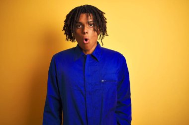 Sarı arka plan üzerinde mekanik üniforma giyen Afro işçi. Şaşırtıcı bir ifade, korku ve heyecan dolu bir yüz ifadesi var..