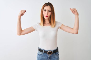 Güzel kızıl saçlı kadın, izole beyaz arka planda duran, silah kaslarını gösteren, gururlu gülümseyen bir tişört giyiyor. Fitness konsepti.