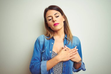 Genç güzel kadın kapalı gözleri ve yüzünde minnettar jest ile göğüs üzerinde elleri ile gülümseyerek izole arka plan üzerinde ayakta. Sağlık kavramı.