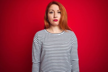 Kızıl saçlı genç bir kadın donanma gömleği giyiyor. Kırmızı izole edilmiş arka plan üzerinde duruyor. Yüzünde ciddi bir ifadeyle rahatlamış. Basit ve doğal bir şekilde kameraya bakıyorsun..