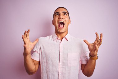 Pembe yalıtılmış arka planda zarif gömlek giyen genç yakışıklı adam çılgın ve kızgın bir şekilde bağırıyor ve agresif bir ifade ve kollarla bağırıyor. Hayal kırıklığı konsepti.