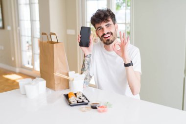 Eve servis yaparken Asya suşisi yiyen ve akıllı telefon ekranı gösteren genç adam parmaklarıyla imza atıyor, mükemmel bir sembol.