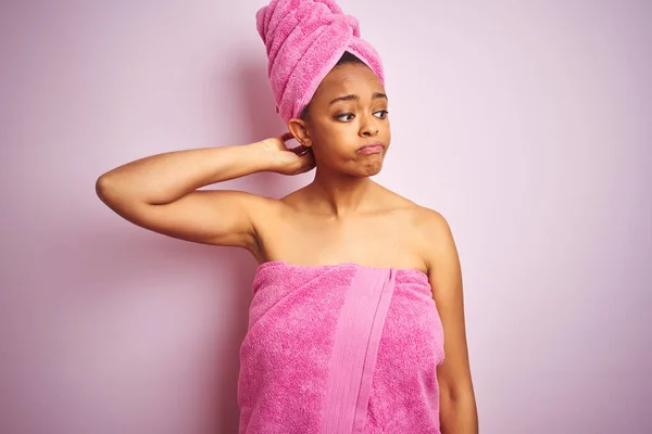 African american woman wearing shower towel after bath over pink isolated background confuse and wonder about question. Uncertain with doubt, thinking with hand on head. Pensive concept.