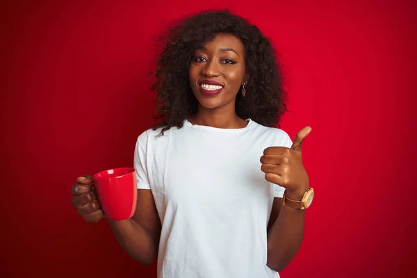 Young african american woman drinking cup of coffee over isolated red background happy with big smile doing ok sign, thumb up with fingers, excellent sign