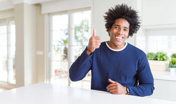 若いアフリカ系アメリカ人の男性は 家庭で幸せな親指を手でジェスチャーを行うカジュアルなセーターを着ている 成功を示すカメラを見て表現を承認する — ストック写真