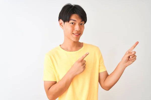 黄色のカジュアルなTシャツを身に着けている中国人男性は 孤立した白い背景笑顔の上に立って カメラを見て2本の手と指で側面を指して — ストック写真