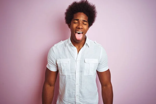身穿白衬衫的非洲裔美国年轻人站在孤立的粉色背景上 带着滑稽的表情伸出舌头 情感概念 — 图库照片