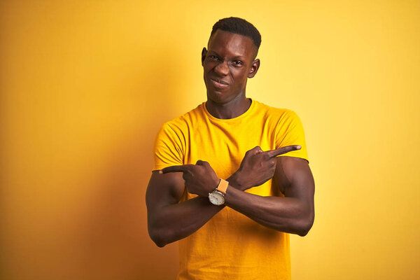 Young african american man wearing casual t-shirt standing over isolated yellow background Pointing to both sides with fingers, different direction disagree