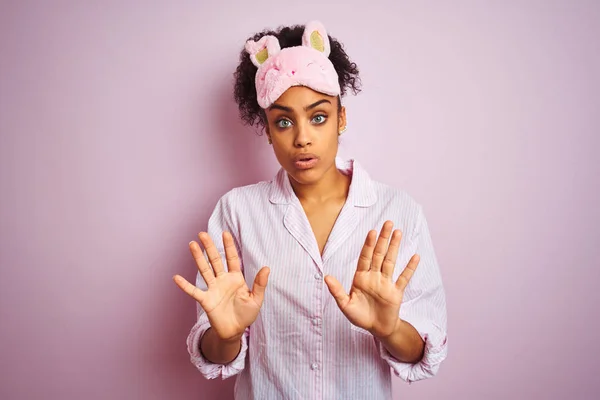 年轻的非洲裔美国女人 戴着睡衣和面罩 披着粉色的孤立背景 手心移开 带着恐惧和恶心的表情 拒绝和否认 停止和禁止 — 图库照片