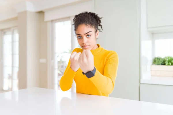 Beautiful african american woman with afro hair wearing a casual yellow sweater Ready to fight with fist defense gesture, angry and upset face, afraid of problem