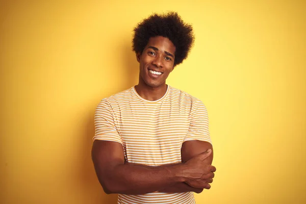 American man with afro hair wearing striped t-shirt standing over isolated yellow background happy face smiling with crossed arms looking at the camera. Positive person.