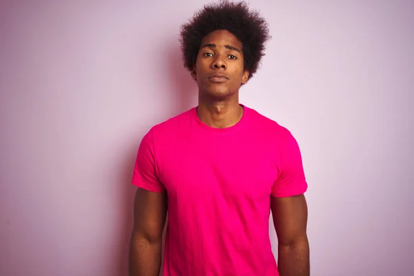 Young american man with afro hair wearing t-shirt standing over isolated pink background with serious expression on face. Simple and natural looking at the camera.
