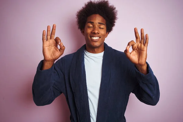 身穿睡衣站在孤立的粉色背景上的年轻的非洲裔美国人放松 闭上双眼微笑 用手指做冥想动作 瑜伽概念 — 图库照片
