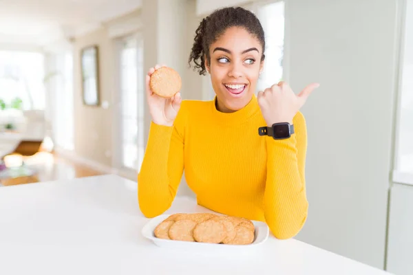 Young african american girl eating healthy whole grain biscuits pointing and showing with thumb up to the side with happy face smiling