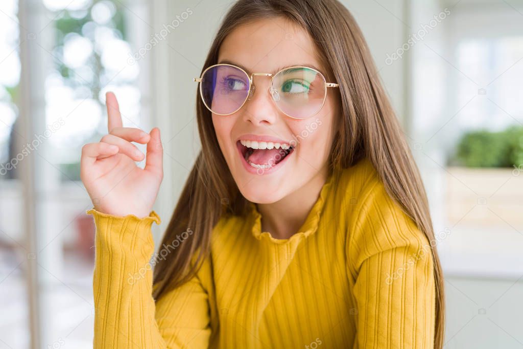 Beautiful young girl kid wearing glasses cheerful with a smile of face pointing with hand and finger up to the side with happy and natural expression on face