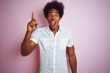 Afro saçlı, beyaz tişörtlü, izole edilmiş pembe arka planda duran genç bir Amerikalı başarılı bir fikri işaret ediyor. Heyecanlı ve mutlu. Bir numara..