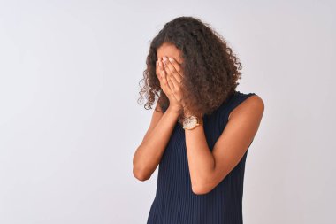 Mavi elbise giyen genç Brezilyalı kadın, izole edilmiş beyaz arka planda dikiliyor. Üzgün yüz ifadesini ellerle örterken ağlıyor. Depresyon kavramı.