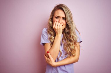 Pembe tişört giyen genç ve güzel bir kadın izole edilmiş arka planda duruyor. Elleri ağız yiyen tırnaklarla gergin ve stresli görünüyor. Endişe sorunu.