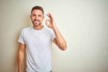 İzole arka plan el ve parmaklar ok işaretiyle yapıyor olumlu gülümseyen üzerinde rahat beyaz t-shirt giyen genç yakışıklı adam. Başarılı ifade.