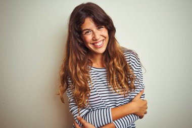 Beyaz izole edilmiş arka plan üzerinde çizgili tişört giyen genç ve güzel bir kadın kollarını kavuşturup kameraya bakarken gülümsüyor. Pozitif kişi.