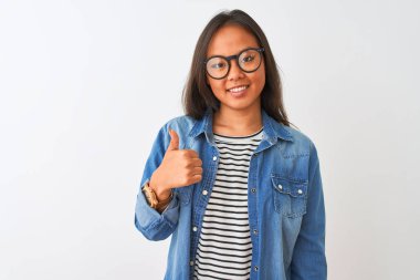 İzole edilmiş beyaz arka plan üzerinde kot gömlek ve gözlük takan genç Çinli kadın mutlu bir el hareketi yapıyor. Kameraya bakıp başarıyı gösteren ifade onaylanıyor.
