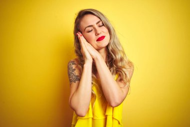 Sarı arka plan üzerinde duran genç saldırgan kadın uyur, yorgun düşler kurar ve elleri ile birlikte poz verir, kapalı gözlerle gülümser..