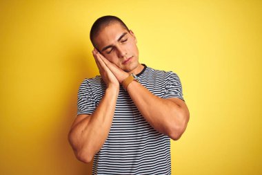 Sarı arka plan üzerinde çizgili tişört giyen yakışıklı genç adam uyur, yorgun düşler kurar ve elleri ile birlikte poz verir, kapalı gözlerle gülümserdi..