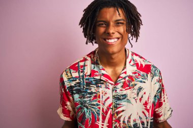 Tatilde saçı rastalı, çiçekli gömlekli, pembe arka planda gezen Afro bir adam. Kollarını kaldırarak ve açık gözlerle başarıyı kutluyor ve şaşırıyor. Kazanan konsept.