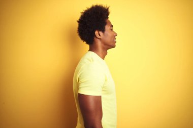 Afro saçlı, yalıtılmış sarı arka plan üzerinde duran, rahat profil pozu veren, kendine güvenen gülümseyen Afro-Amerikan bir adam..