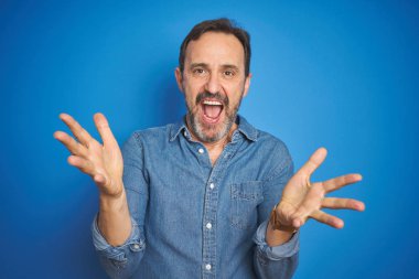 Yakışıklı, orta yaşlı, gri saçlı, mavi arka planda, neşeli gülümseyen, yardım eli uzatan ve kabul gören yaşlı bir adam..