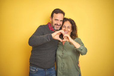 Izole sarı arka plan üzerinde güzel orta yaş çift elleri ile kalp sembolü şekli yapıyor aşk gülümseyerek. Romantik kavram.