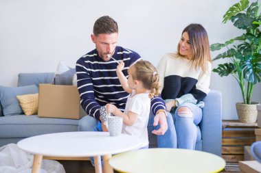 Güzel aile, anne-babalar kanepede kahve içme oturmuş karton kutular etrafında yeni evde oynayan çocuğuna bakıyor