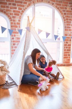 Güzel öğretmen ve yeni yürümeye başlayan kız yerde oturmuş anaokulunda tek boynuzlu at ve oyuncak bebekle oynuyor.