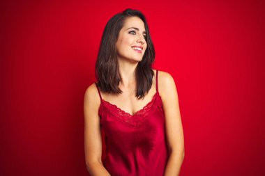 Kırmızı izole edilmiş arka plan üzerinde seksi iç çamaşırları giyen genç ve güzel bir kadın yüzünde gülümseme, doğal bir ifade ile yan yana bakıyor. Kendinden emin gülen.